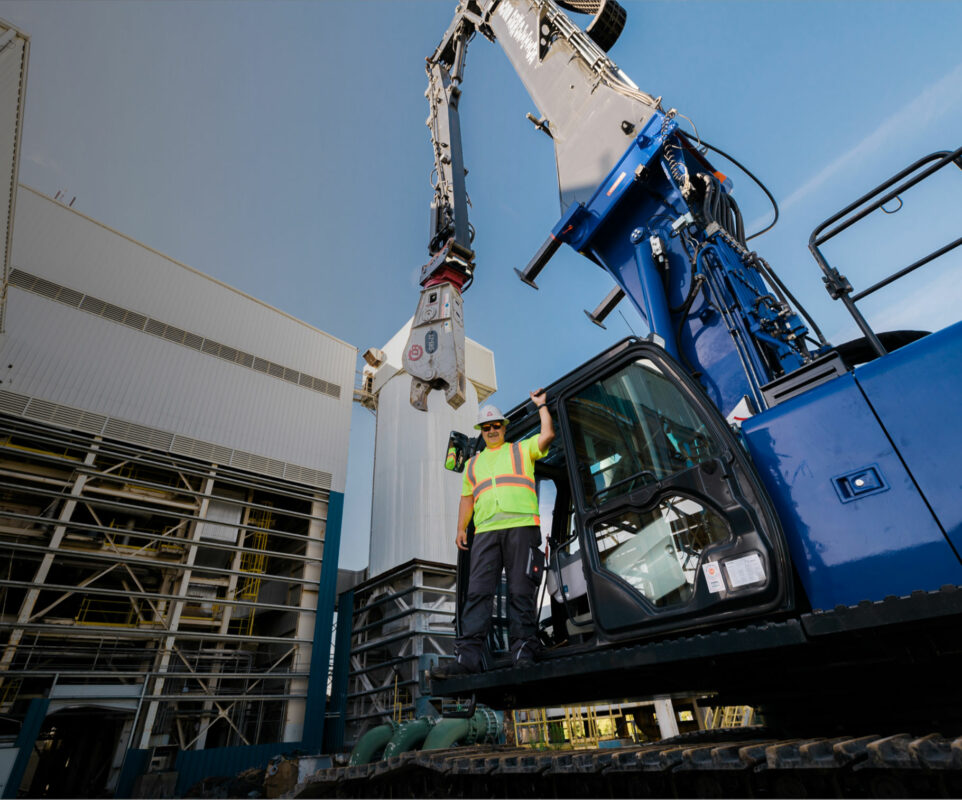 Worker directing large demo equipment on construction site.