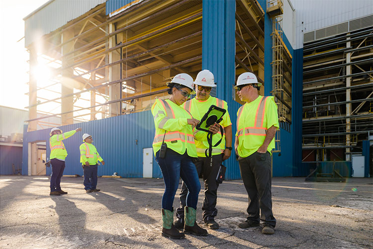 3 construction workers in safety vests talking at an outdoor job site