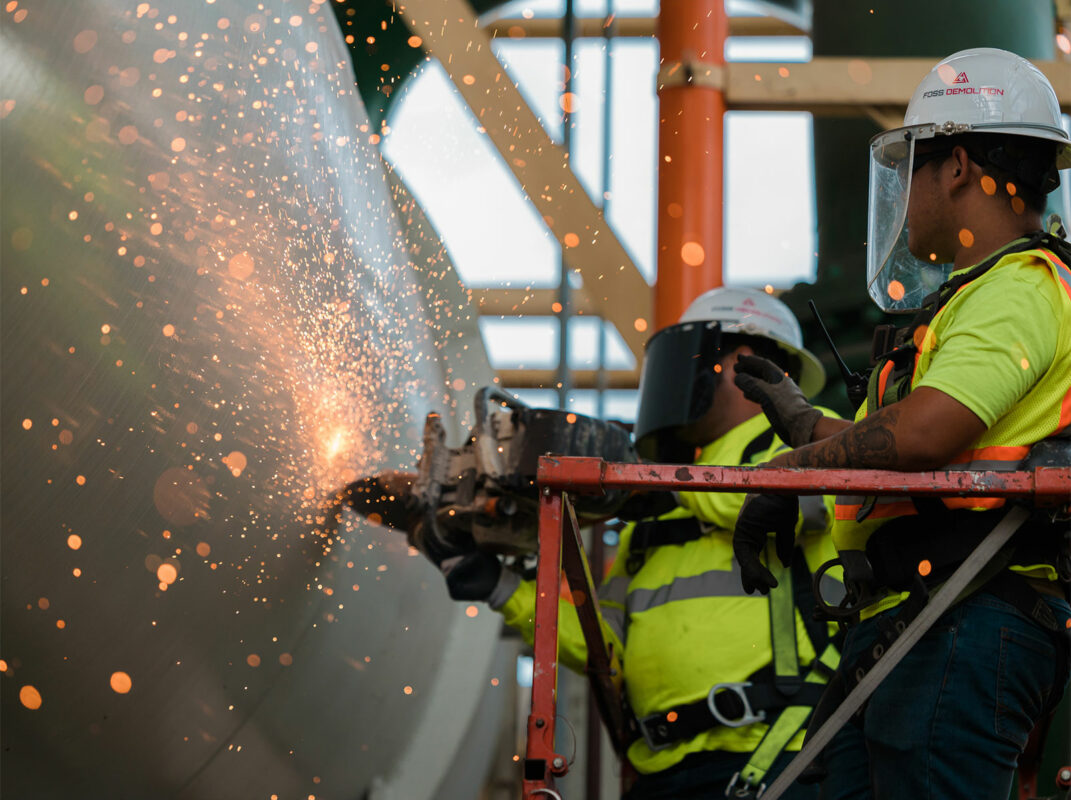 Men in safety gear on lift cutting metal with sparks